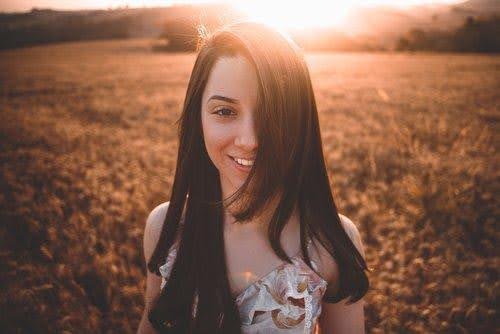 a close up of a brunette woman looking at the camera as she stands in a field