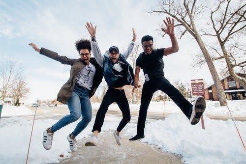 three friends jumping into the air with appendages extended shouting for joy in a snowy space